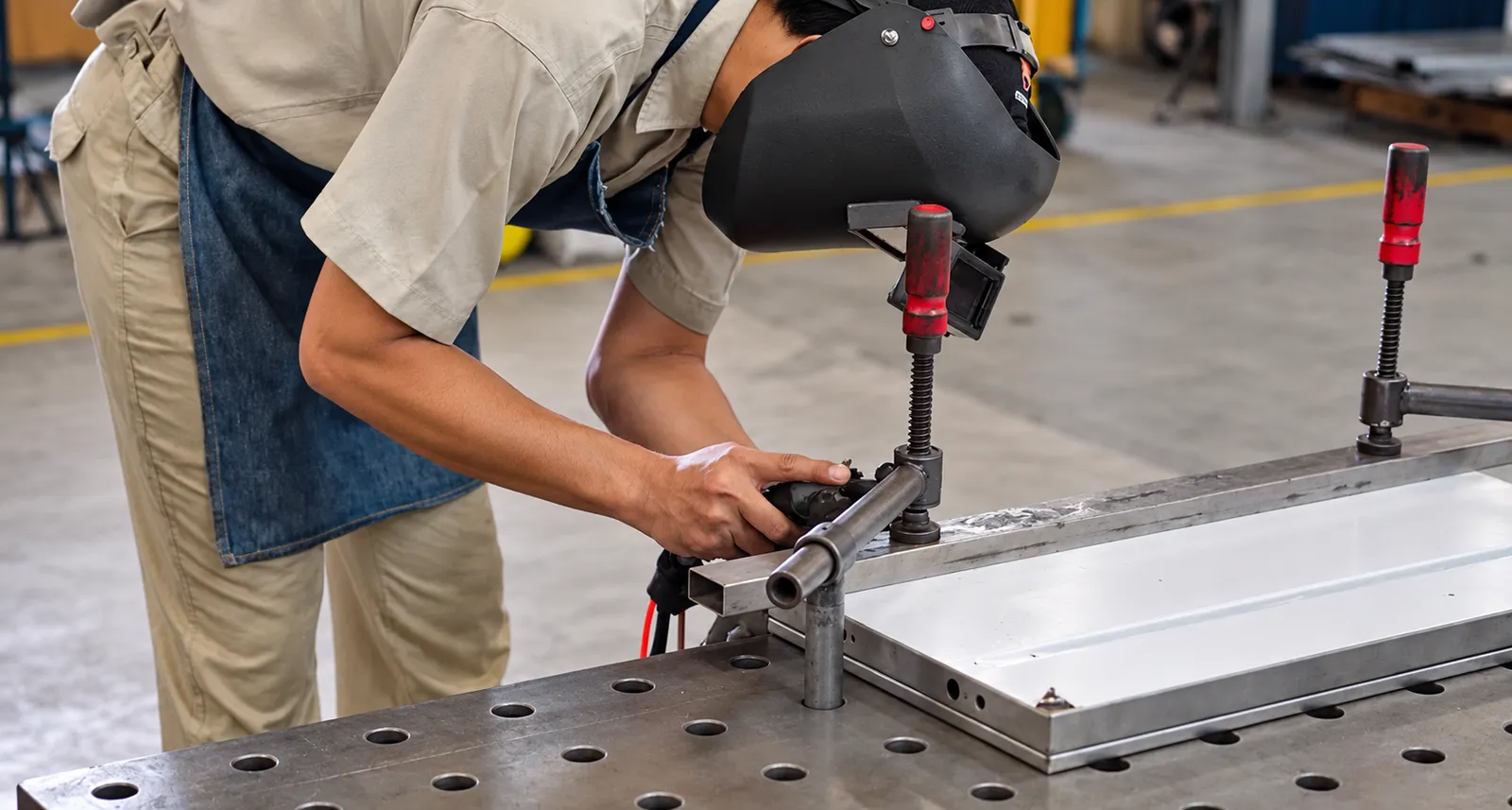 A welder at a jig table in the workshop, clamping a stainless steel frame
